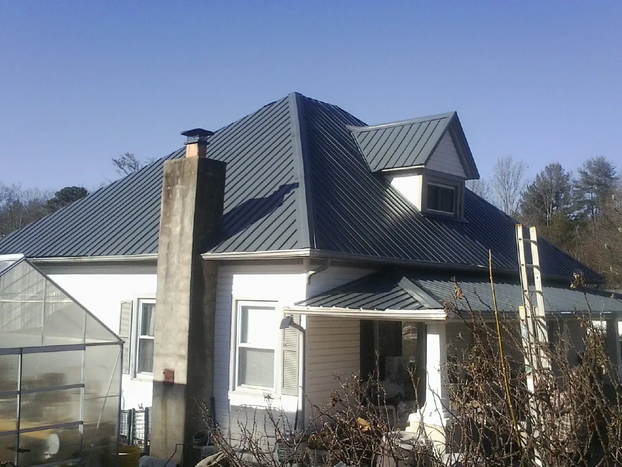 Dark blue standing seam metal roof on a white farmhouse with dormer — Slate & Tile Roof Repair by Roofing Brothers in Croswell