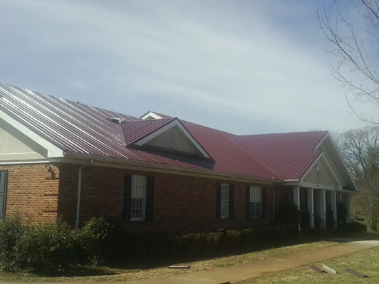 Red metal roof with gabled entries on a long brick building, from a Hail Damage Roof Repair job in Croswell