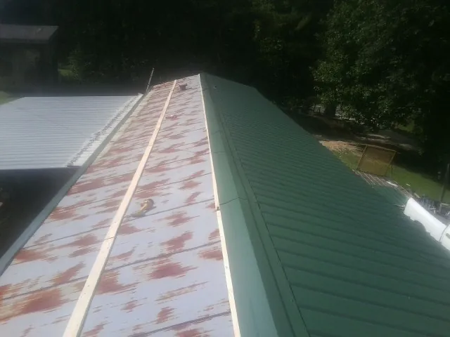 Old rusted panels beside newly installed green metal roofing — Wind Damage Roof Repair by Roofing Brothers in Croswell