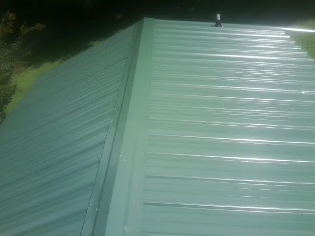 New green metal panels meeting at the ridge of a roof — Flat Roof Repair work by our crew in Croswell