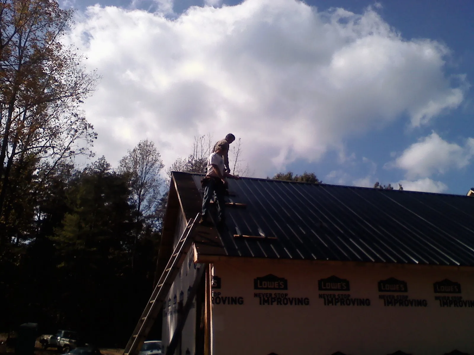 Roofer fastening dark metal panels high against a cloudy sky, from a Roof Inspection job in Croswell