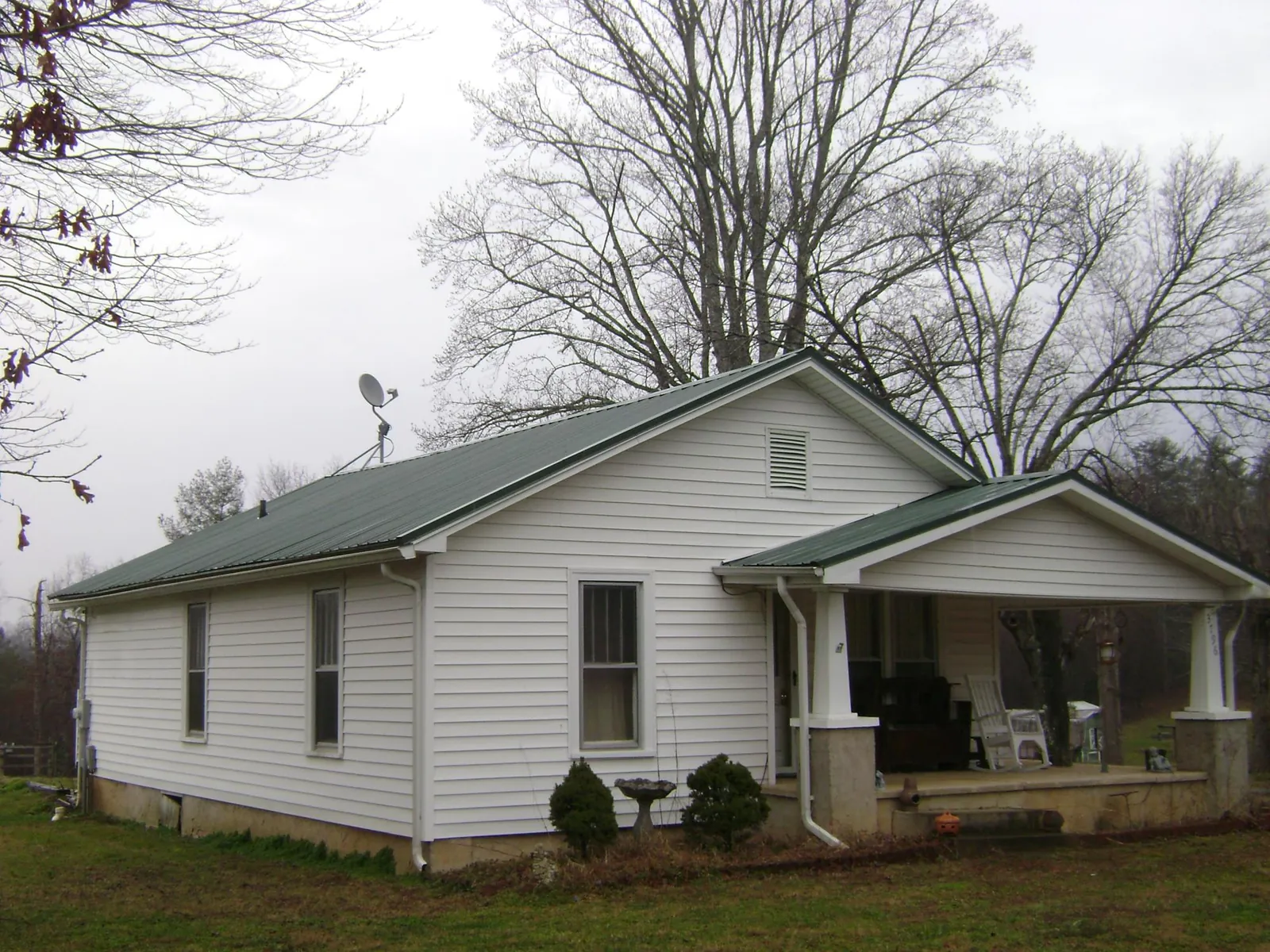 Green metal roof on a white bungalow with a side porch in Croswell