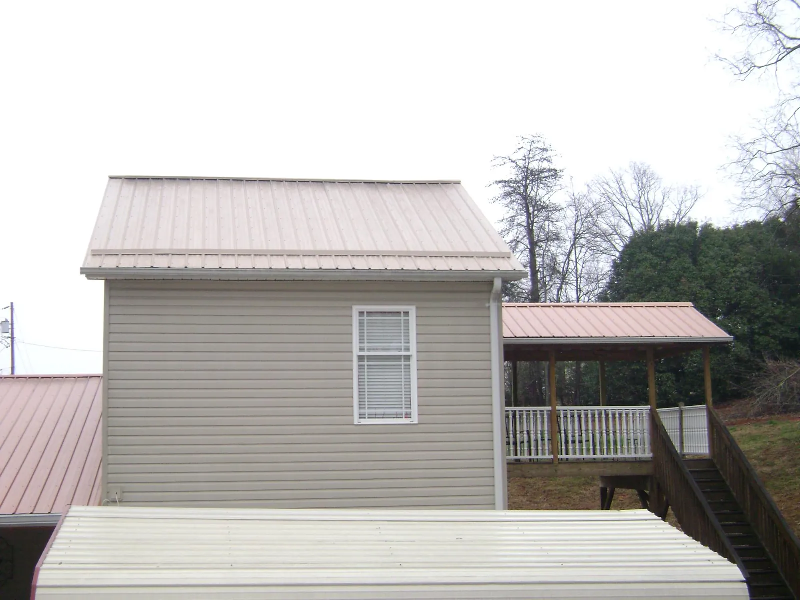 Tan metal roofs on a two story addition and attached porch, from a Roof Replacement job in Croswell
