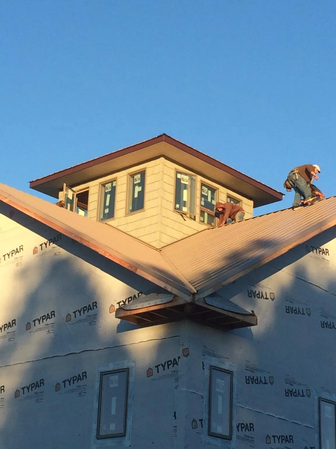 Roofers working around a rooftop cupola on a new metal roof at sunset — Roof Waterproofing in Croswell by Roofing Brothers